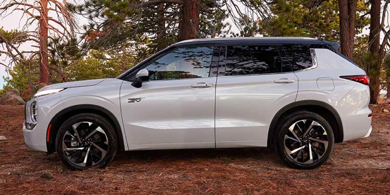 A white Mitsubishi Outlander PHEV parked on a dirt road with trees in the backround.