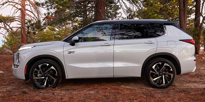 A white Mitsubishi PHEV parked on a dirt road with a forest in the background.