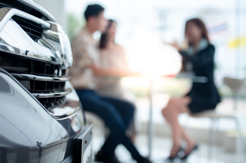 Three individuals sitting in a car dealership discussing a car sale.