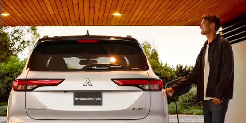 A man plugging in his silver 2025 Mitsubishi Outlander Plug-in Hybrid.