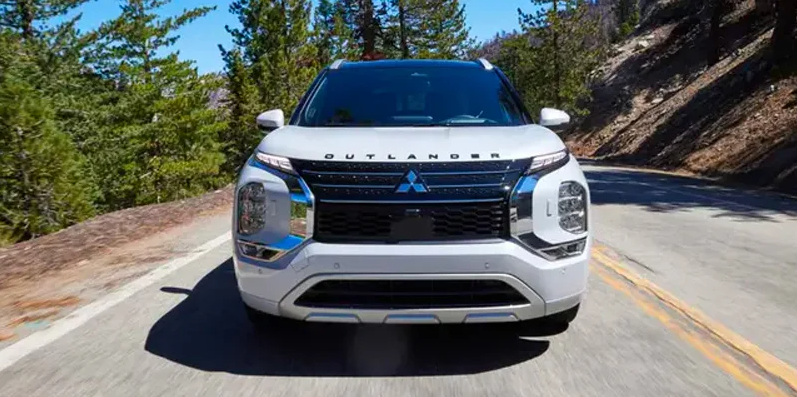 A white Mitsubishi Outlander PHEV driving down the road.